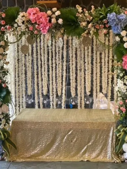 This setup combines sparkle and flowers for a truly festive look. The gold sequin cloth and colorful floral frame make it perfect for Navratri or Diwali.