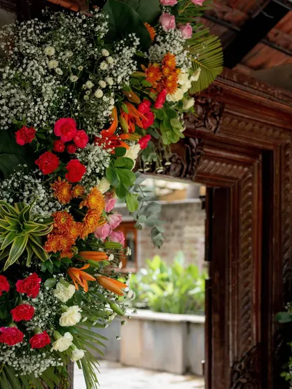 A close-up of the vibrant floral arrangements framing a traditional carved wooden doorway, showcasing the rich colors and textures used in the Mehendi decor.