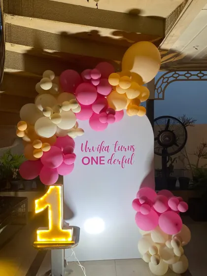 A simple yet beautiful "ONEderful" first birthday setup. The clean white backdrop is accented with a pink and peach balloon garland and a glowing marquee number one.