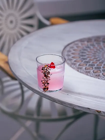 The Rosa Fresca, a vision in pink, sits on a mosaic table. This cocktail is a story of romance, blending gin, rose, spice, and honey. It’s a testament to the love stories that unfold within my mansion’s walls.