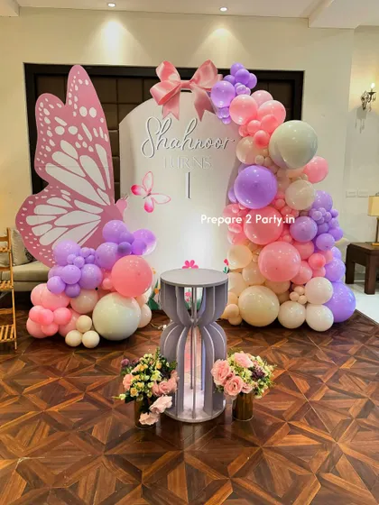An elegant butterfly theme for a first birthday. This beautiful setup features a large butterfly wing for photos, a custom arch backdrop, and a pastel balloon garland in pink, purple, and cream.