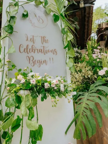A welcome sign surrounded by lush green foliage and delicate white and pink flowers.