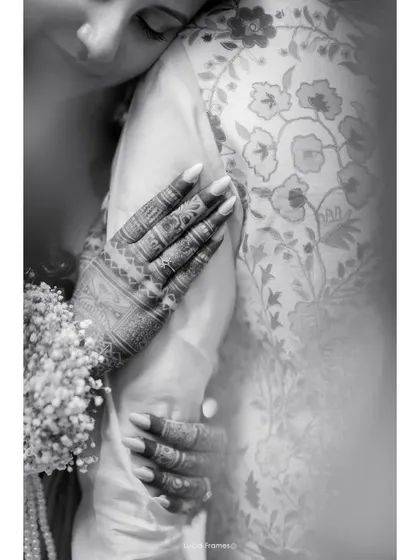 A beautiful black and white detail shot, focusing on the bride's henna-adorned hands as she embraces the groom.