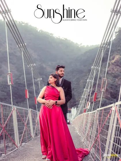 An elegant portrait of a couple on a suspension bridge, the woman in a vibrant pink gown, creating a striking contrast with the natural surroundings.