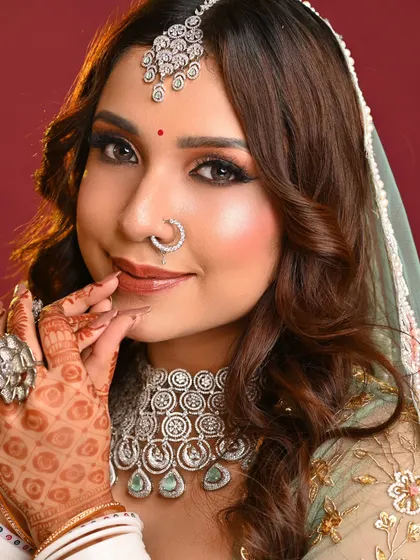 This shot captures the complete look, showcasing the flawless base, defined eyes, and how the makeup complements the pastel green outfit and heavy diamond jewelry.