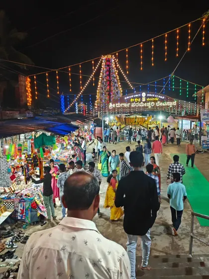 The festive atmosphere outside a temple in Mangalore during a jatre, with colorful lights and bustling crowds.