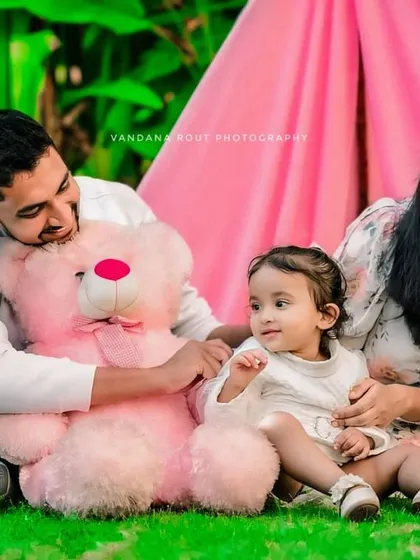 A sweet family moment during an outdoor picnic-themed shoot. The parents and their child interact with a giant teddy bear, creating a charming and memorable family portrait.