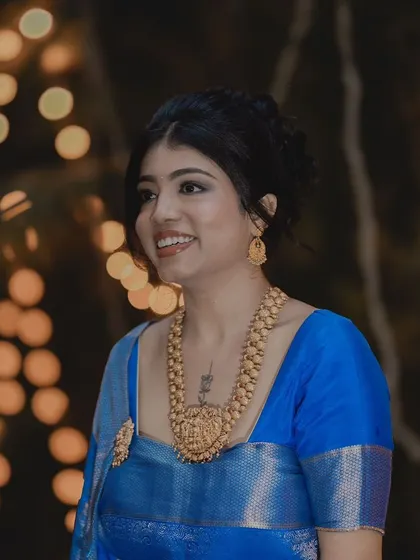 A portrait of a bride in a striking royal blue silk saree. Her makeup is glamorous, with a smokey eye and a neutral lip, and her hair is styled in a chic updo.
