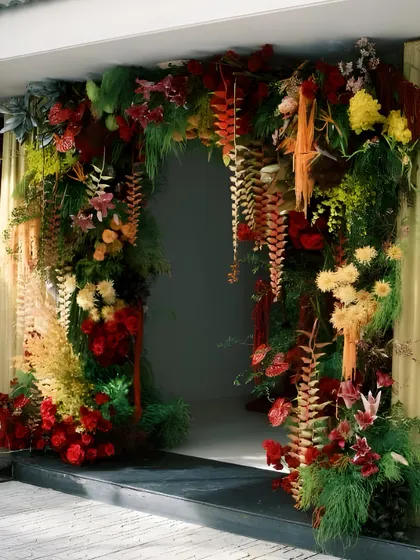 A lush and dramatic floral archway, overflowing with tropical leaves and vibrant red and yellow flowers. This creates a stunning entrance or photo backdrop for a tropical-themed event.