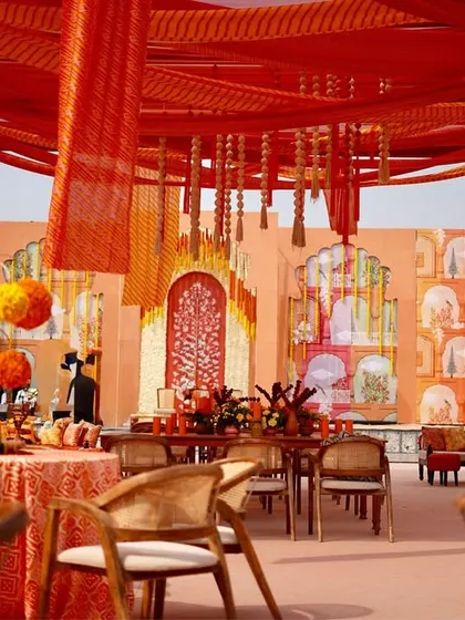 The guest seating area under a canopy of red and orange drapes. The tables are set with traditional block-print tablecloths and marigold centerpieces, perfectly capturing the Rajasthani vibe.