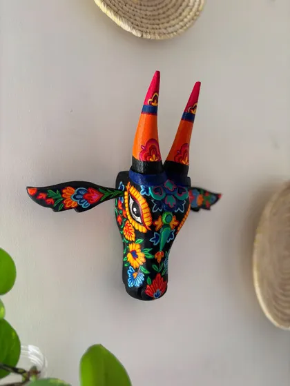This wall-mounted Nandi head is a celebration of Kashmiri 'aari' embroidery, translated into paint. The vibrant floral motifs on a black background create a stunning contrast that immediately draws the eye.