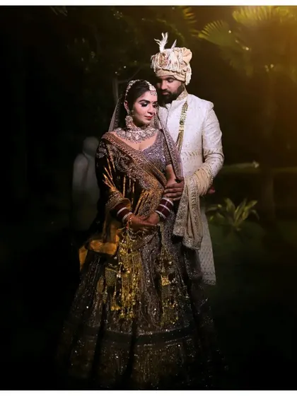 A stunning night portrait of the wedding couple. The dramatic lighting highlights the intricate details of the bride's lehenga and the groom's sherwani, creating a royal and elegant look.