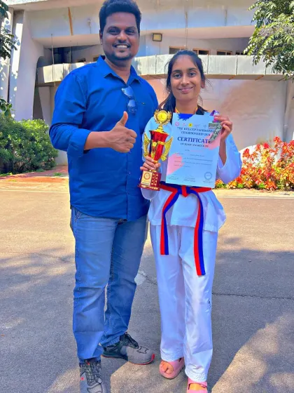 This student gives a thumbs-up, celebrating her win at the Taekwondo championship with her trophy and certificate.