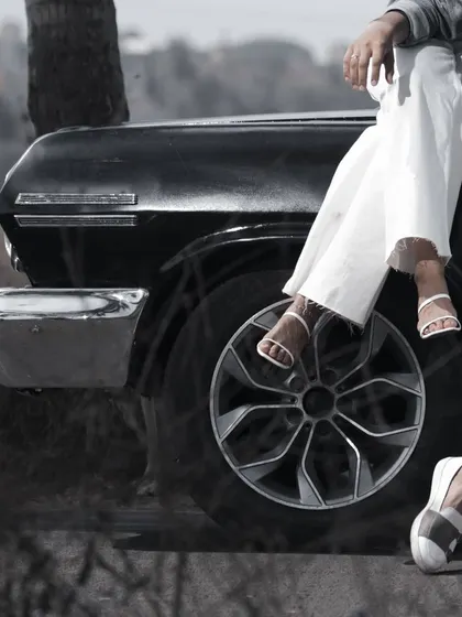 A close-up, black and white detail shot of a couple's legs and shoes as they sit on the hood of a classic car. This creative angle adds a stylish, editorial feel to the pre-wedding gallery.
