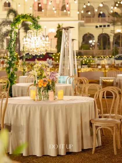 A view of the elegant round table setup at the Jaipur night wedding. Each table featured a low floral centerpiece, candlelight, and a stunning backdrop of hanging chandeliers and lush greenery.