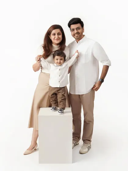A full-length family studio portrait with the parents standing on either side of their young son, who is proudly standing on a white block.