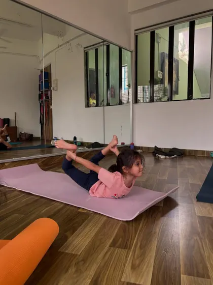 A young girl holds a strong Dhanurasana, or Bow Pose, in the studio. This pose builds great back strength.