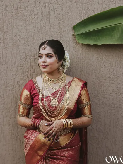 A classic portrait of a South Indian bride in her red silk saree, adorned with layers of traditional gold jewellery.