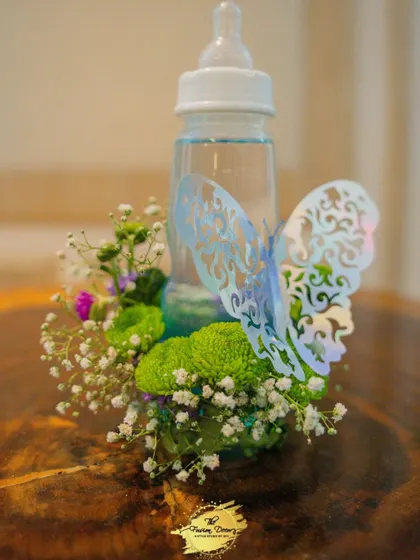A simple yet creative centerpiece idea for a baby shower. I used a baby feeding bottle as a vase, surrounding it with fresh baby's breath and green chrysanthemums, and finished it with a delicate butterfly cutout for a touch of whimsy.