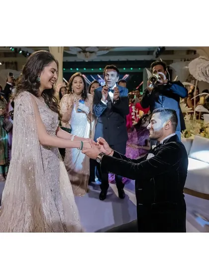 Raghav goes down on one knee to put a ring on Sanjana's finger. The surprise and joy on her face, along with the cheering crowd, make this a perfect proposal moment.