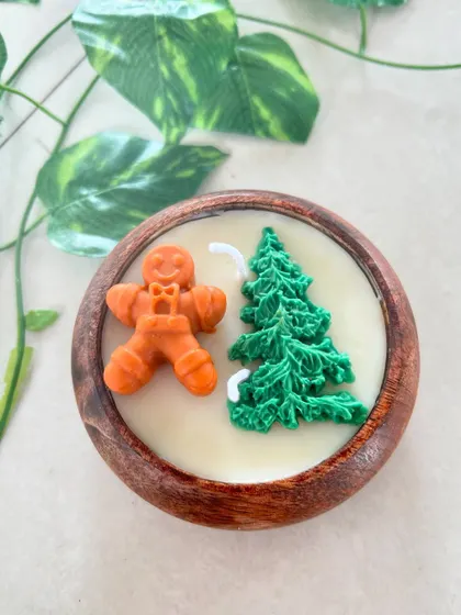 A Christmas candle featuring a gingerbread man and a green tree in a wooden bowl.