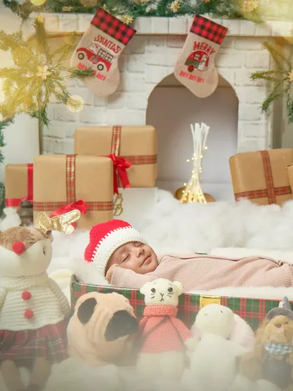 A wide view of the newborn Christmas setup, with the baby sleeping peacefully in a gift box surrounded by festive toys and a warm fireplace.