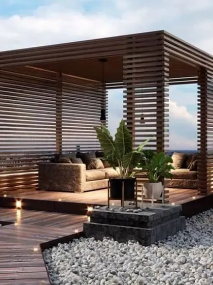 A luxurious rooftop lounge built within a custom wooden slat pergola. This design provides privacy and shade while maintaining an open, airy feel, perfect for creating an elegant outdoor seating area with integrated floor and pendant lighting.