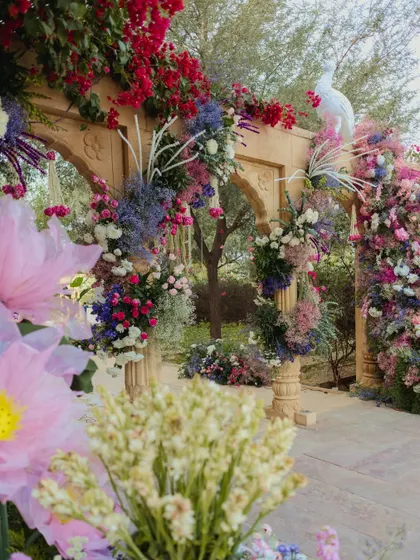 A stunning floral archway in shades of purple and pink, with a white peacock perched atop, creating a fairytale entrance for the wedding ceremony.