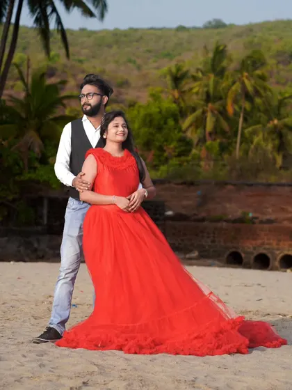 A relaxed and stylish pose on the beach. The groom's casual vest and jeans combo pairs nicely with the bride's dramatic red ruffled gown.