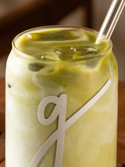 A close-up of the iced matcha latte, showing the texture and the brand's logo on the glass.
