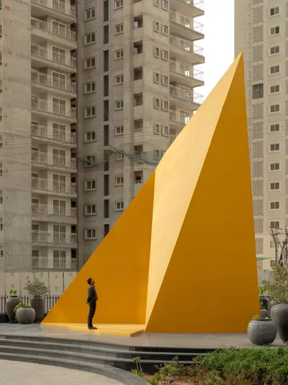 The "Yello" is an homage to the human condition, with its folded facets representing the different journeys and experiences that shape an individual. This view, with a person standing within its frame, highlights the sculpture's human scale and interactive nature.