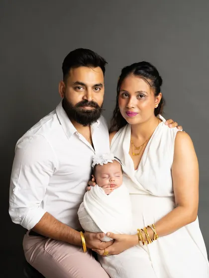 A classic studio portrait of a new family of three. The parents proudly hold their swaddled newborn, a perfect first family photo to cherish forever.