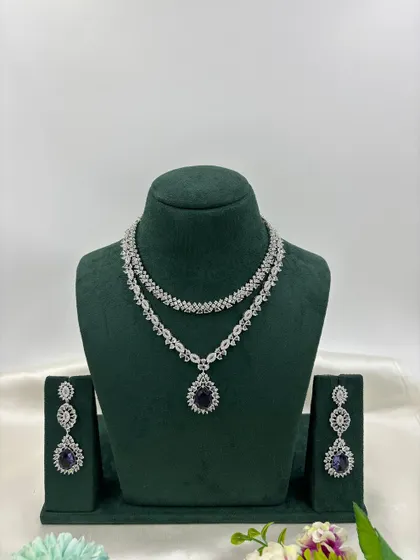 A graceful double-layered AD necklace. The top layer is a simple floral chain, while the bottom layer features a pear-shaped pendant. It is available in white, pink, green, and blue stones.