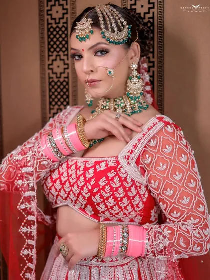 A classic portrait against a patterned wall. The bride's direct gaze and poised posture exude confidence and grace, making her red and white lehenga shine.