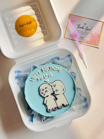 A cute and intimate bento cake design showing two stick figures sharing a kiss, with the message "Happy Birthday My Love" on a soft blue background.
