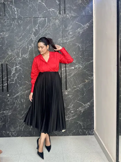 Power dressing with a feminine twist. A bold red shirt tucked into a black pleated midi skirt, paired with classic black pumps, creates a look that's perfect for the office or a formal event.