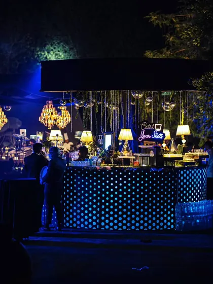 A wide view of the party, centered around a quirky polka-dot bar decorated with hanging disco balls and table lamps, all under a canopy of blue light.