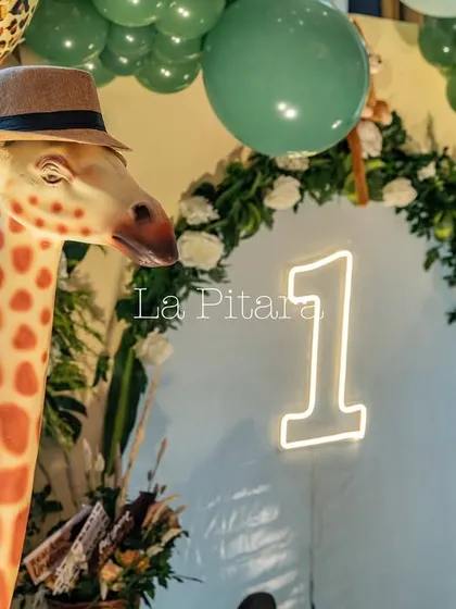 A giraffe prop wearing a safari hat next to a neon '1' sign, marking a stylish and fun first birthday celebration.
