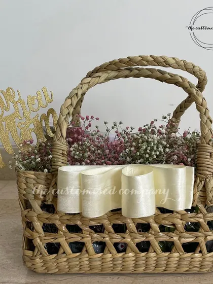 A beautiful and simple arrangement featuring baby's breath in a woven jute basket, accented with a concept bow and a "Love You Mom" cake topper. We can create custom floral concepts for any occasion.
