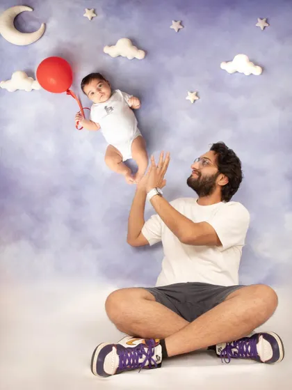 Daddy, daddy cool! A fun and creative shot showing a proud father playing with his levitating baby, held up by a single red balloon.