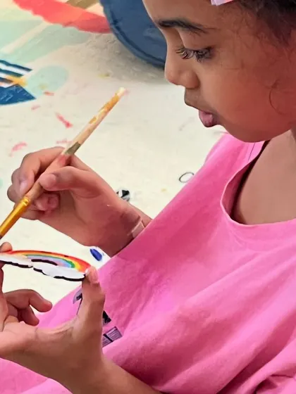 The careful concentration of a child painting a rainbow onto her wooden cutout. It's amazing to watch their fine motor skills and creativity in action.