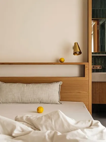 This bedroom in Apartment 1005 showcases our custom bed design with an integrated headboard shelf. The space is connected to an ensuite bathroom with vibrant green tiles, adding a pop of color to the otherwise neutral palette.