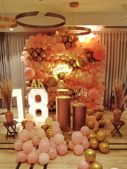 A glamorous 18th birthday party with a full wall of pink and rose gold balloons, marquee numbers, and elegant pedestals.