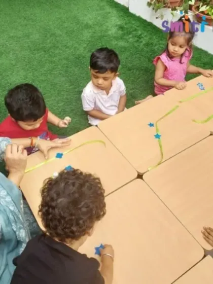 An overhead view of a teacher and children working on their Rakhi crafts. Our outdoor spaces are often used for hands-on activities, connecting learning with nature.