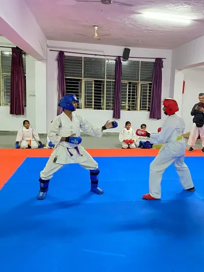 Students face off in a controlled sparring match, wearing red (aka) and blue (ao) protective gear, just like in an official WKF tournament setting.