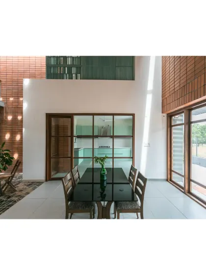 The dining space in 'An Earthy Affair' is framed by the rich texture of exposed brick and the clean lines of a modern kitchen. Sunlight filters through the double-height volume, highlighting the honest material palette and creating a warm, inviting atmosphere for family meals.