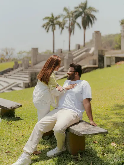 A relaxed and intimate moment on a stone bench in a park, surrounded by palm trees and sunshine.