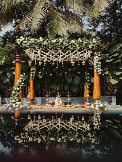 A stunning poolside mandap setup, with traditional wooden pillars and white floral decor beautifully reflected in the water. My team and I transform venues to create breathtaking backdrops for your ceremony.