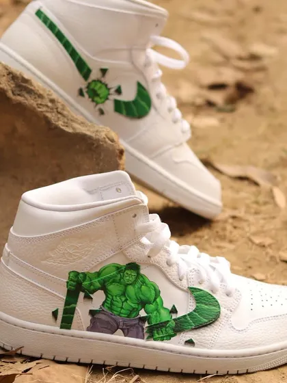 A full shot of the custom Hulk Air Jordan 1s. One shoe features the Hulk smashing the swoosh, while the other shows his fist breaking through, creating a dynamic and cohesive pair.
