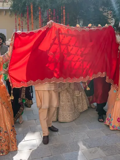 A unique wedding entry where the groom is hidden under a red cloth held by family members.
